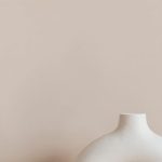 Home Studio Maintenance - White ceramic vase in creative shape of ring placed on white marble stand against beige wall as home decoration element or art object