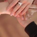 Equalization - Top view of faceless friends in different clothes stacking hands together while standing on wooden floor indoor on sunny day