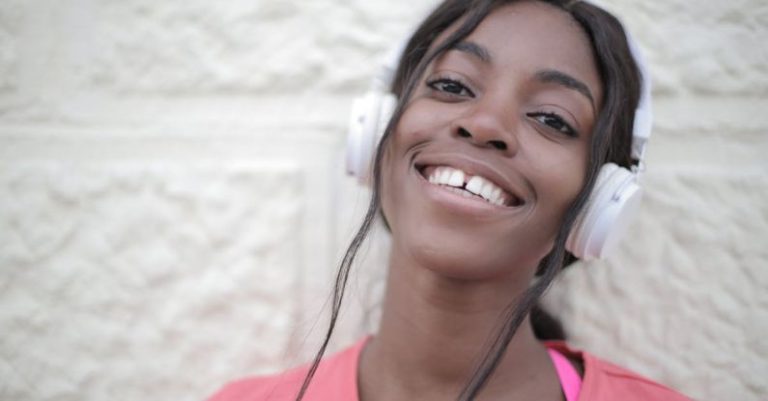 Wireless Audio - Positive young black female in bright t shirt wearing headphones and listening to music while looking at camera