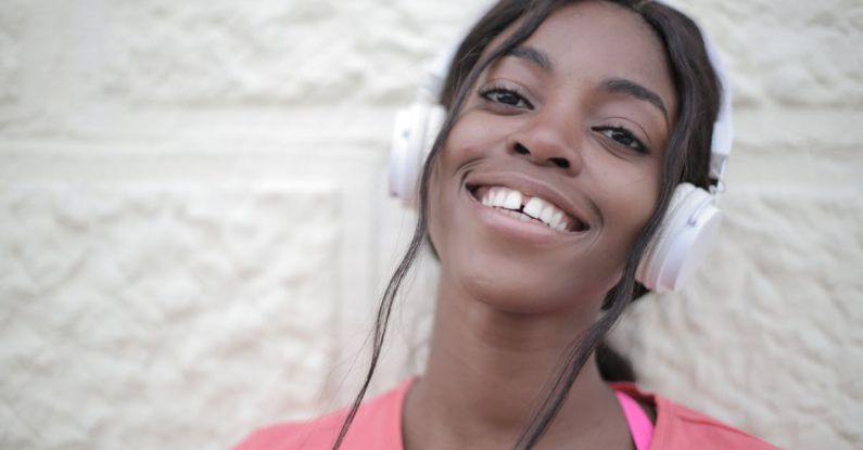 Wireless Audio - Positive young black female in bright t shirt wearing headphones and listening to music while looking at camera