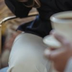 Speaker Placement - Crop anonymous female host talking to guest and having coffee while recording conversation on microphone