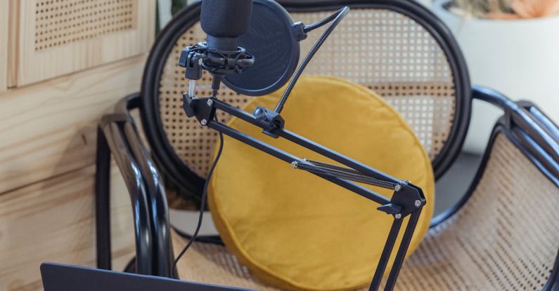 Digital Audio Formats - Modern laptop and microphone on tripod placed near wicker chair in modern studio before recording podcast