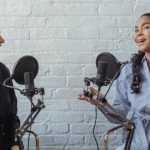 Podcast Hosting - Smiling African American female guest gesticulating while having interview with journalist sitting near mic