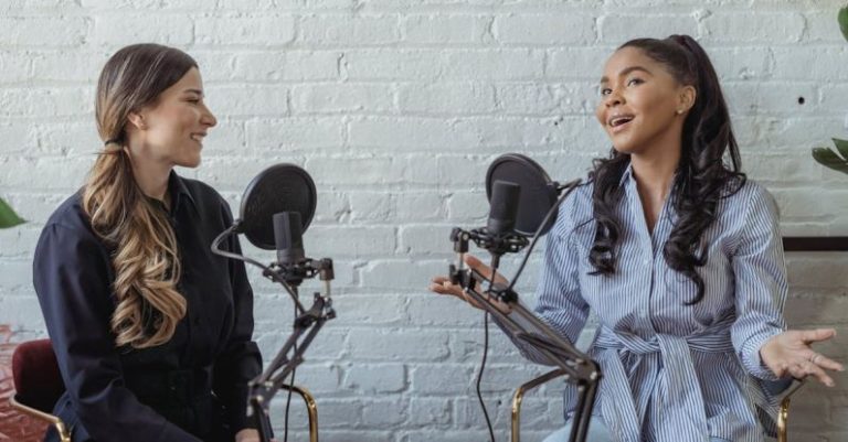 Podcast Hosting - Smiling African American female guest gesticulating while having interview with journalist sitting near mic